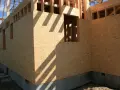 Budowa domu z płyt OSB. Konstrukcja drewniana z widocznymi otworami okiennymi i drzwiami. Cień belek pada na ściany.