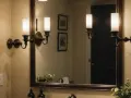 Eleganckie kinkiety z mlecznymi kloszami zamontowane są nad lustrem, tworząc przytulną atmosferę.