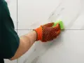 Rękawica z gąbką czyści białe płytki, pokazując, jak usunąć zaschnięty klej do płytek.
