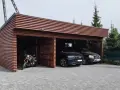 Drewniana wiata na samochód przed domem, chroniąca dwa czarne SUV-y i motocykl.