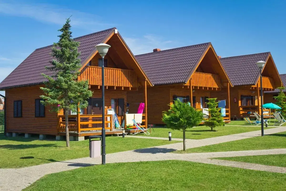 Gotowy domek letniskowy całoroczny, z drewnianą elewacją i balkonem, stoi na zielonym trawniku.