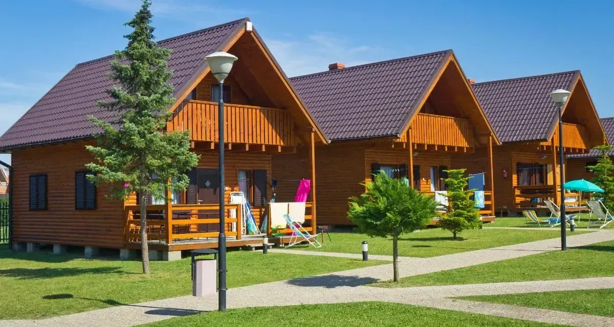 Gotowy domek letniskowy całoroczny, z drewnianą elewacją i balkonem, stoi na zielonym trawniku.