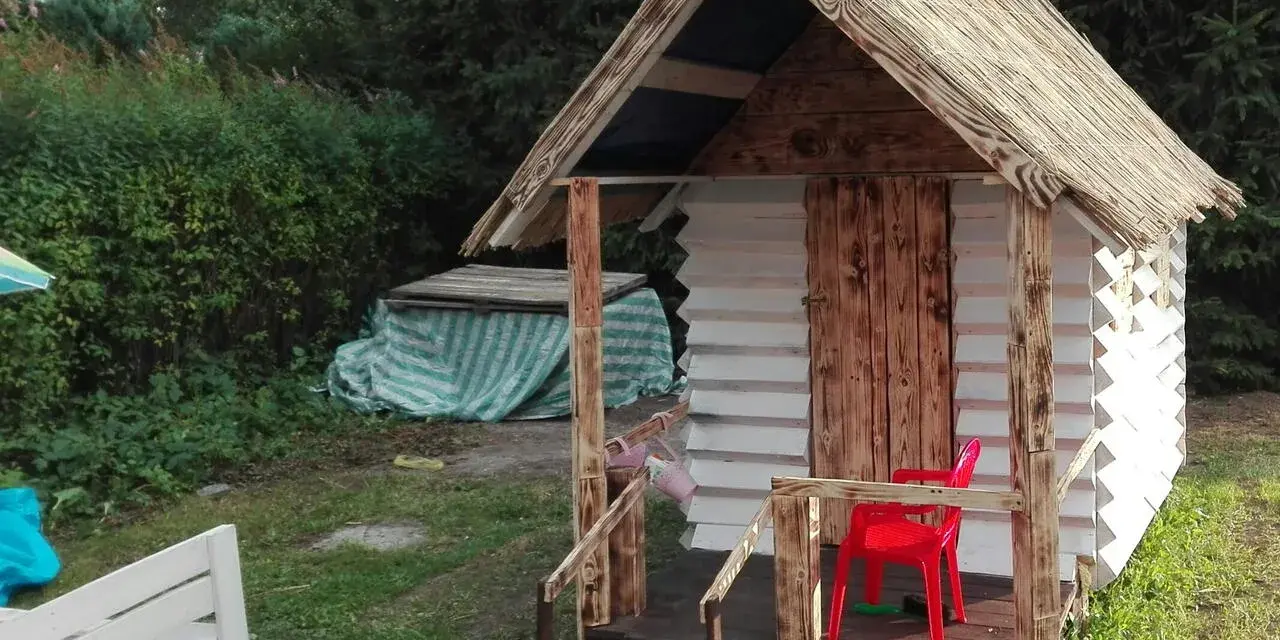 Domek dla dzieci z palet, z drewnianymi drzwiami i słomianym dachem, gotowy na zabawę.
