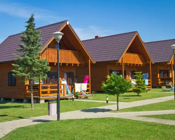 Gotowy domek letniskowy całoroczny, z drewnianą elewacją i balkonem, stoi na zielonym trawniku.