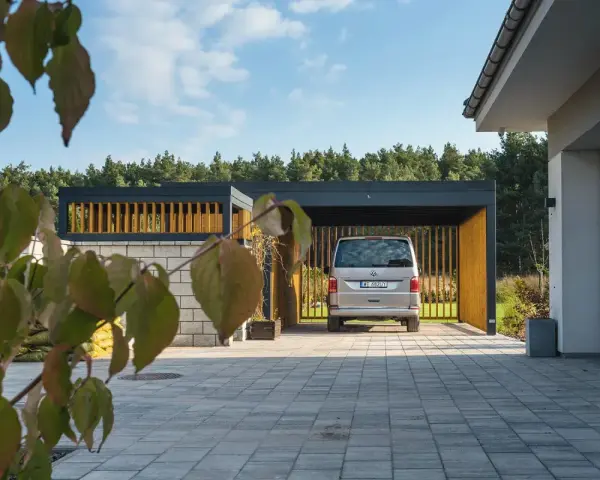 Nowoczesna wiata garażowa zabudowana z drewnianymi elementami i srebrnym vanem.