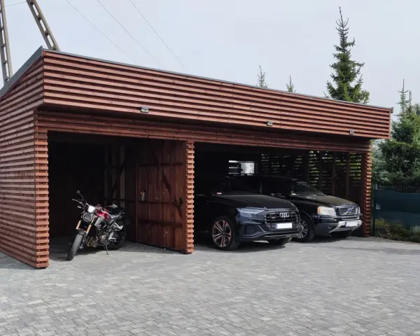 Drewniana wiata na samochód przed domem, chroniąca dwa czarne SUV-y i motocykl.