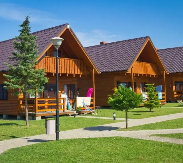 Gotowy domek letniskowy całoroczny, z drewnianą elewacją i balkonem, stoi na zielonym trawniku.