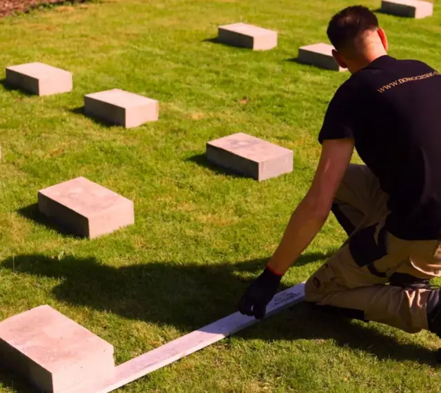 Ustawianie bloczków betonowych na trawniku to pierwszy krok, jak zrobić podłoże pod domek ogrodowy. Precyzyjne rozmieszczenie to klucz do stabilnej konstrukcji.