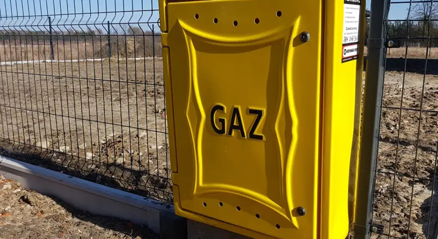 Żółta skrzynka gazowa z napisem "GAZ" przy ogrodzeniu. Zastanawiasz się, ile kosztuje przyłącze gazu?