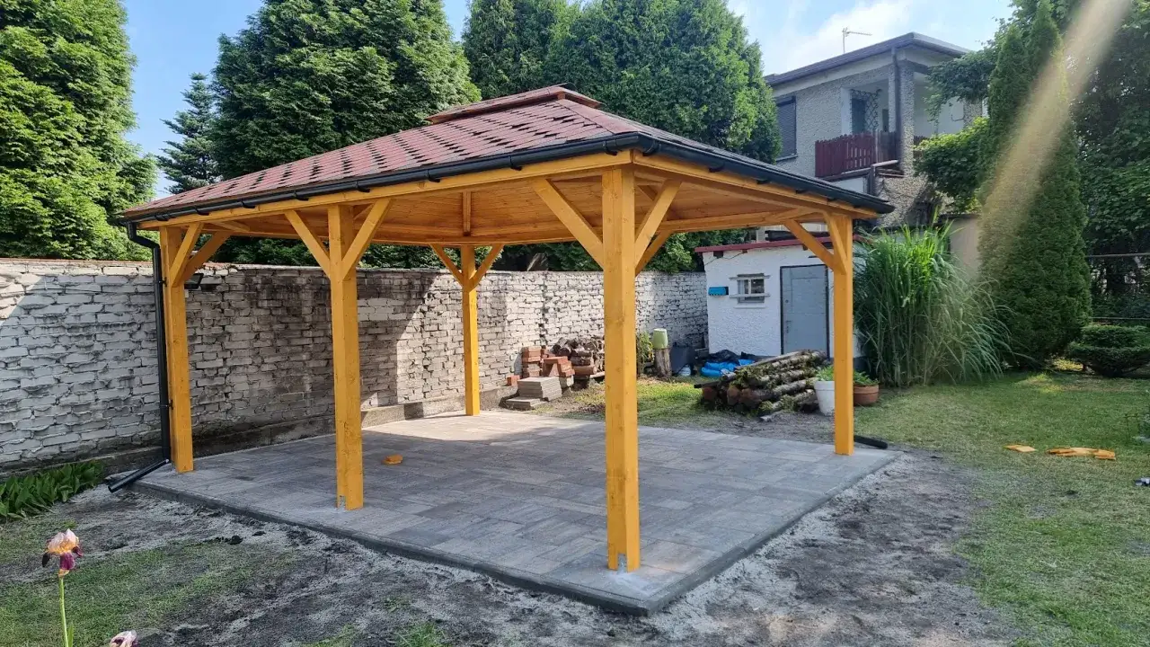 Nowa altana ogrodowa z podłogą z kostki brukowej, otoczona zielenią i murem. Idealne miejsce na relaks.