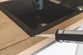 Pistolet z silikonem aplikuje uszczelnienie wokół zlewu, pokazując, jak polożyć silikon na blacie kuchennym.