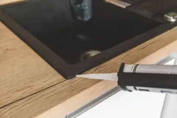 Pistolet z silikonem aplikuje uszczelnienie wokół zlewu, pokazując, jak polożyć silikon na blacie kuchennym.
