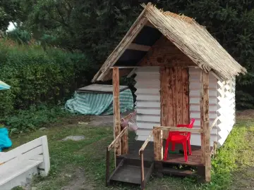 Domek dla dzieci z palet, z drewnianymi drzwiami i słomianym dachem, gotowy na zabawę.